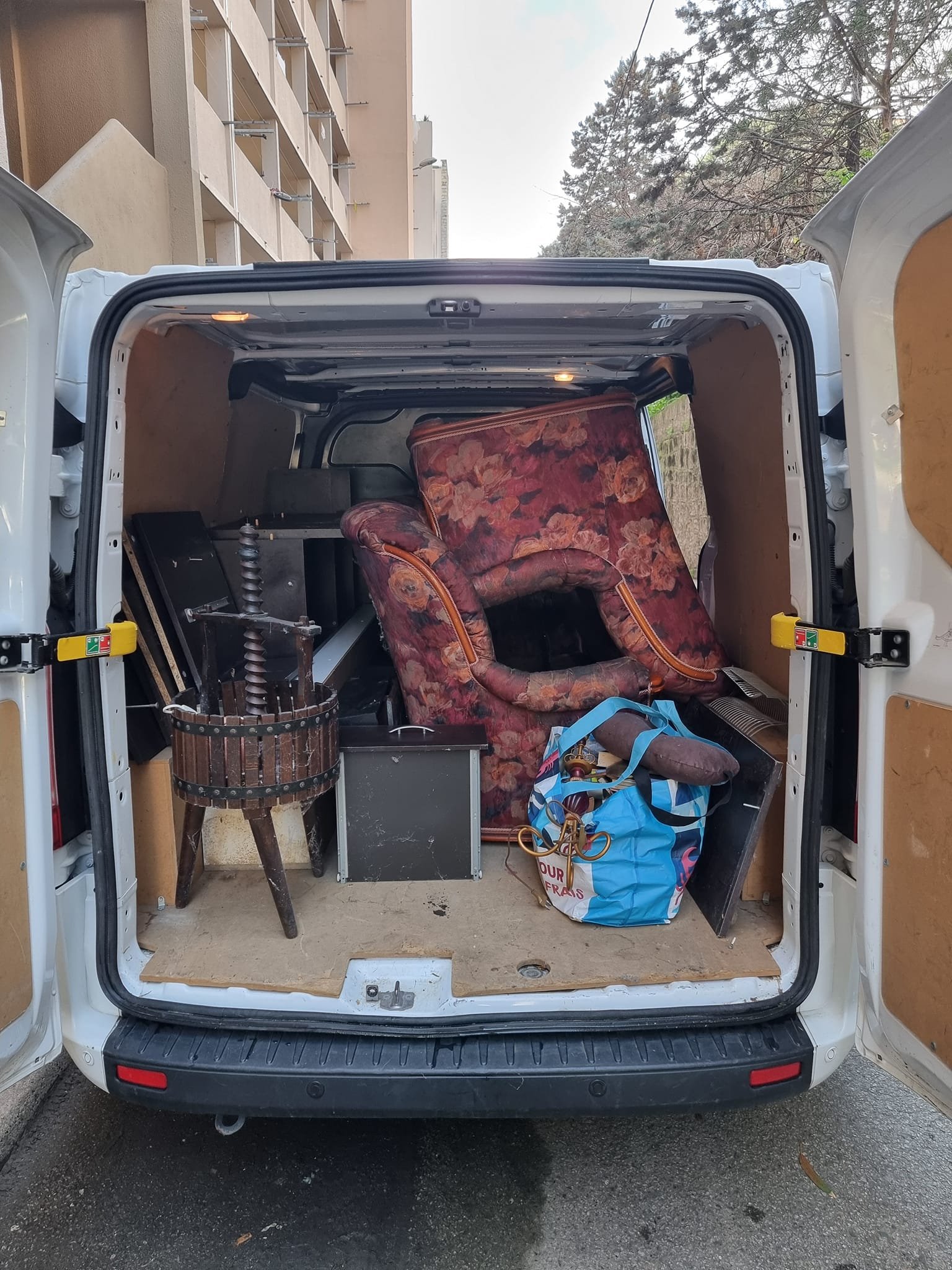 Contenu d’un utilitaire rempli de meubles et d’objets divers, dont deux fauteuils empilés, une table basse, un tonneau en bois et un sac de transport.
