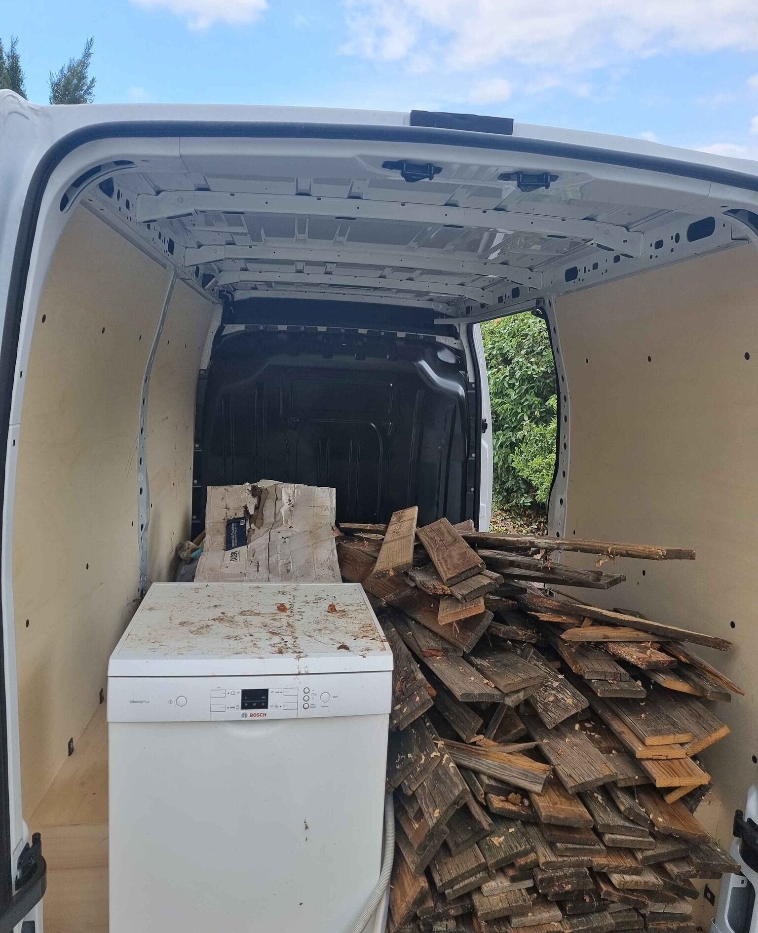 Chargement d’un utilitaire avec un lave-vaisselle et un gros tas de bois usagé, destiné à la déchetterie ou au recyclage.